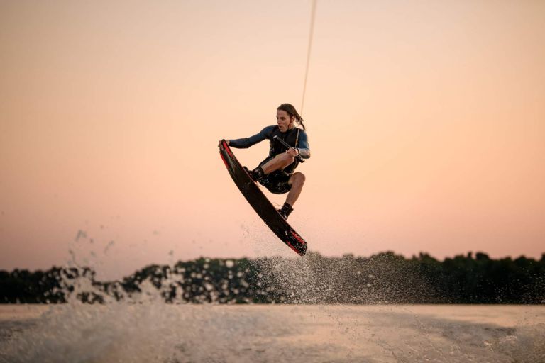 active strong man making trick in jump time with wakeboard on sky background. Summertime watersports activity